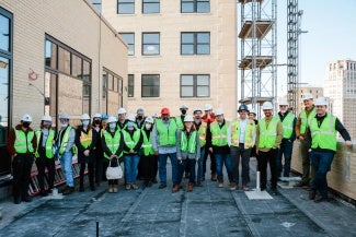 A group of people in visibility vests and hard hats stand for a photo on a balcony. 