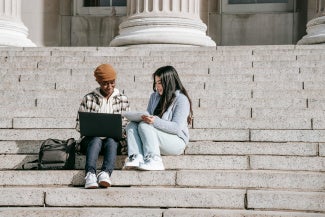 two students sitting on steps looking at laptop