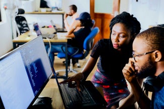 two coworkers leaning over a computer screen collaborating