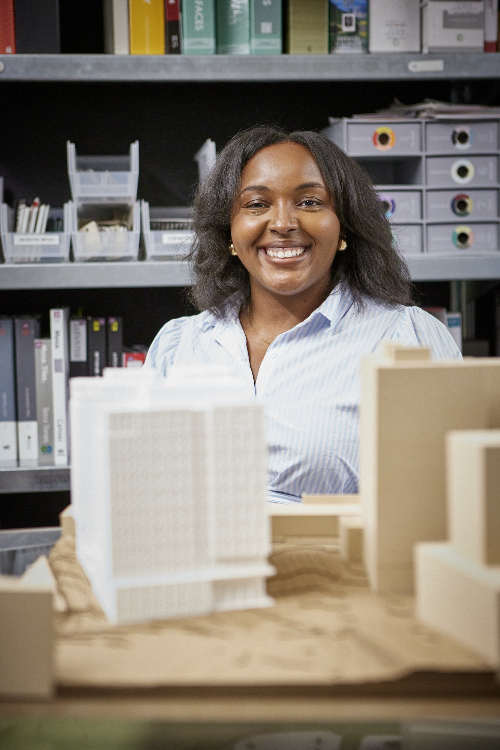 Young, Black, female architect smiling over her building models.