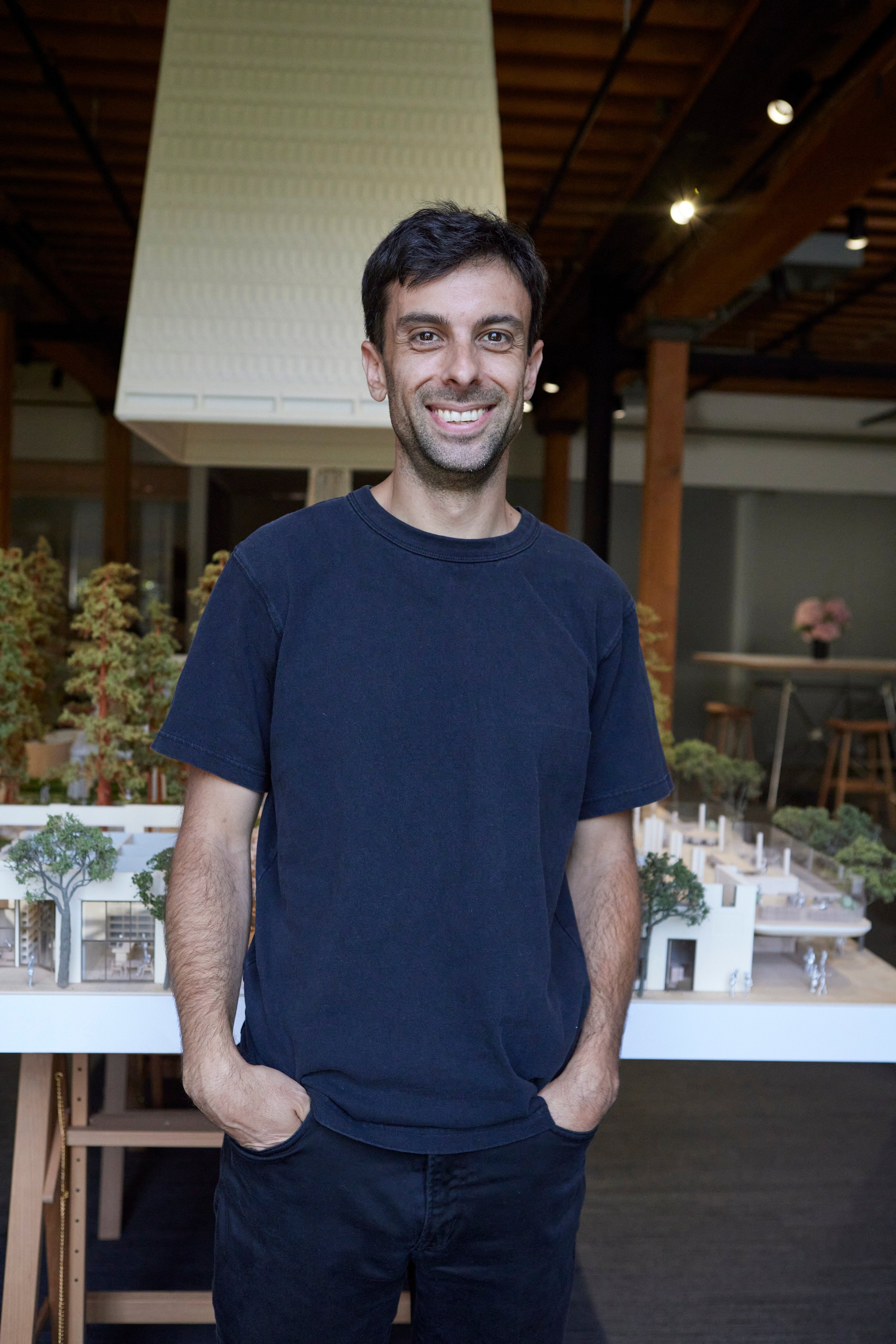 Medium-skinned architect smiling in front of architectural model.
