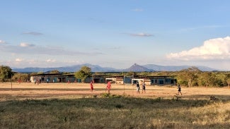 kids play in front of a structure in an open field with mountains and trees in background