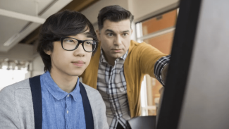 Young person looking at a computer while another person looks over their shoulder
