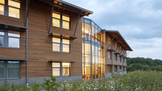 building with wooden facade lit up from inside in a field of green plants