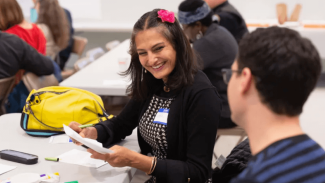 Smiling woman sitting at a table at an event wearing a name tag 
