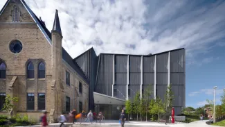 people walk past a building that is both historic and modern