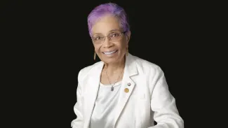 Headshot of a woman in a white suit with purple hair