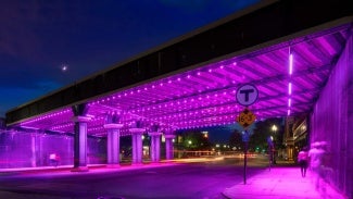 People walking through an underpass at night lit with purple light