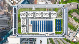 A bird's eye view of the top of a building in a city, outfitted with solar panels and greenery