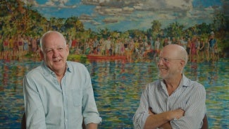 Two men in button down shirts are talking in front of a watercolor painting.