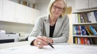 Woman looking at blueprint with hand holding pen in foreground