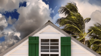 peak of home with storm clouds and palm trees blowing in wind behind