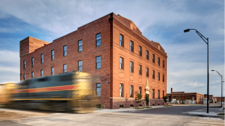 corner of a brick building with a train in motion going by