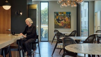 Resident sits at high-top table with lower tables and chairs behind her. 