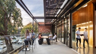 View from DPR Sacramento Zero Net Energy Office looking west on exterior terrace showing large operable window wall, solar shade trellis and view to existing trees and J street