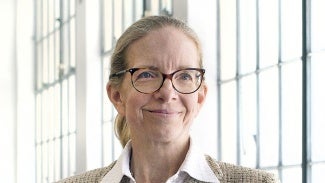 headshot of Elizabeth Plater-Zyberk; woman standing in front of windows wearing glasses with her hair pulled back