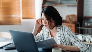 Young Asian woman handling home finances with laptop, looking worried while going through financial bills. Financial plan, tax, spending and budgets, financial problems concept