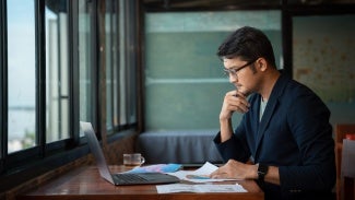 Asian young businessman working with laptop at office, office worker browsing in laptop for necessary information. 