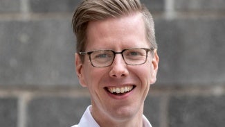 headshot of a man with short blonde hair wearing glasses and a white shirt. 