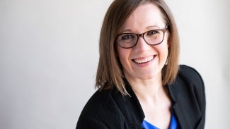 Headshot of a woman with short brown hair wearing glasses and a dark jacket 