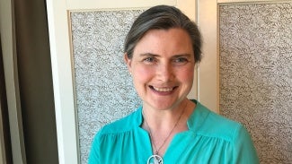 A woman in a teal top stands in front of a decorative shade.