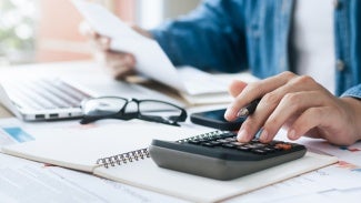Image of arms/torso sitting at a desk and using a calculator