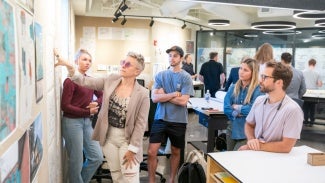 architecture students point at blueprints on a wall