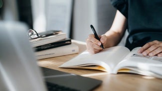 Cropped shot of focused young Asian woman reading book and making notes at home, concentrates on her studies. Further education, continuous learning concept - stock photo