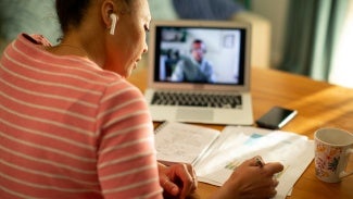 Woman taking notes as she watches a class on her laptop computer