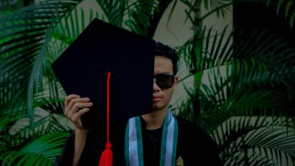 Man holding Master's graduate cap in front of his face
