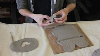 Hands forming clay pottery on a work table
