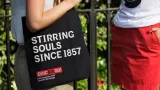 Person holding a tote bag that reads "Stirring Souls Since 1857"