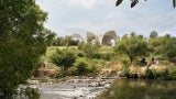 View across a river toward a concrete pavilion nestled in the landscape