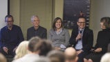 View from the audience of a panel of speakers; one is holding a microphone