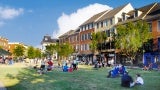 Residents sit on the community green on a sunny day; multifamily housing faces the park.