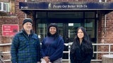 A man and two women stand in front of a brick care center with a navy awning.