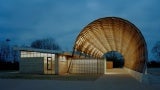 Building exterior at dusk. The building has a large curved canopy. 