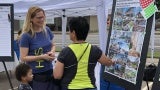 A woman talks to an adult and a child at an outdoor information kiosk. 