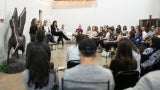 A panel of four women give a presentation in front of an audience in a white-walled gallery space next to a Pegasus statue.