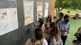 Students write on a chalkboard attached to a building’s brick exterior. 