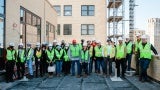 A group of people in visibility vests and hard hats stand for a photo on a balcony. 