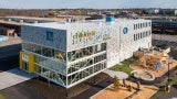 Arial shot of a children's museum at daytime. There is a wooden play structure in the foreground. 