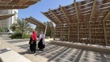 Two women in hijab walk under a woven canopy. 