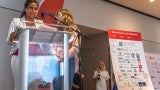 Two women stand behind a transparent lectern at a conference.