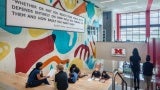 Students sit on bleacher steps next to a wall mural with an inspirational quote.