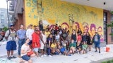 A group of people in front of an external wall mural they have been working on. 
