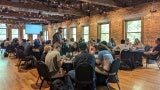 People sit at round tables in a room with exposed brick walls. 