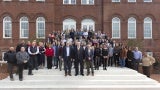 a large group of people stand on the steps in front of a brick building.