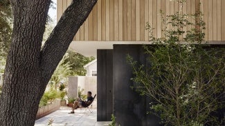 Man on patio of West Campus Residence with trees in foreground. 