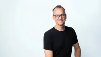 Headshot of a man in a black shirt and glasses